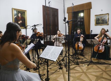 Fotografia. Koncert we wnętrzu Willi Decjusza. Muzycy grają na skrzypcach i wiolonczeli w Sali Balowej.